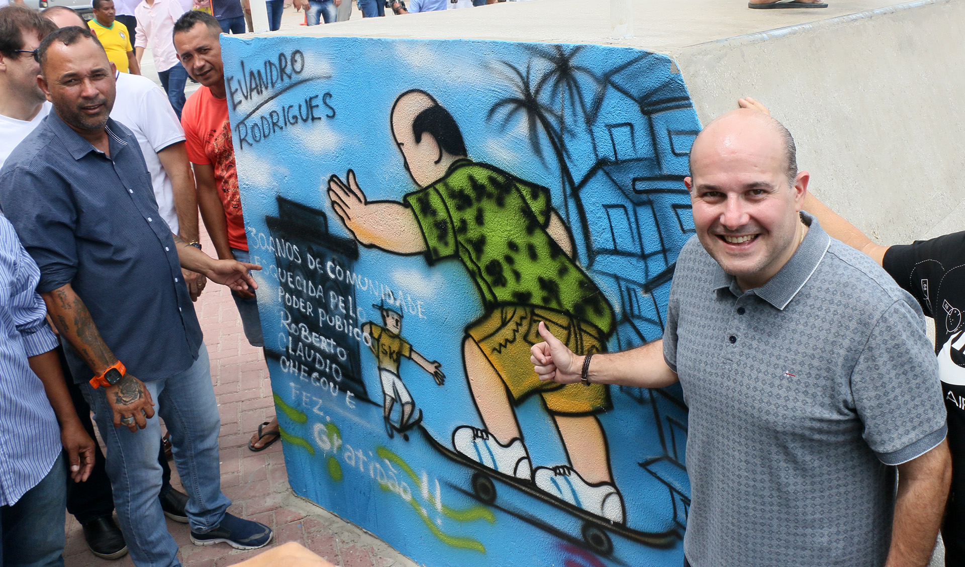 prefeito roberto claudio posa ao lado de um painel com um desenho dele, feito por um artista local para agradecer pela reforma da praça